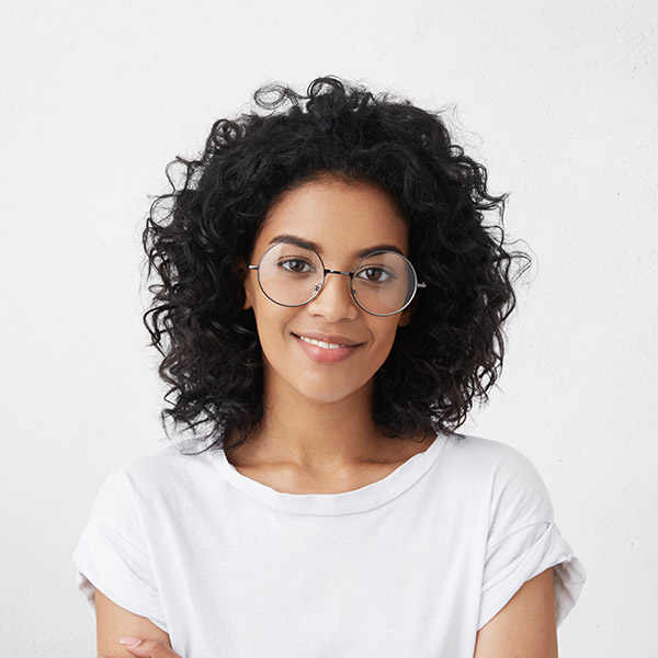 Close up studio shot of beautiful young mixed race woman model with curly dark hair looking at camera with charming cute smile while posing against white blank copy space wall for your content